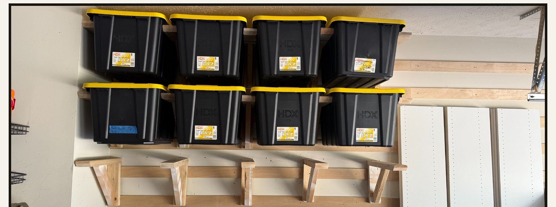 Custom 12-tote garage storage wall built from pine with black HDX totes with yellow lids hanging on a French cleat rail